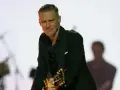 Bryan Adams w czarnym garniturze gra na gitarze. Sprawdź jego nadchodzące wydarzenia i koncerty.