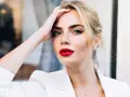 Frau mit roten Lippen und weißem Blazer, Hand am Kopf.