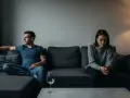 Para siedzi na kanapie w milczeniu, oddzielona pustką. Widać wyraźny stashing w związku, brak komunikacji i emocjonalne oddalenie.