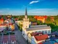 Słoneczny rynek w Bytowie z kościołem i zamkiem w tle. Kolorowe kamienice tworzą urokliwy krajobraz.