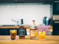 Zwei Flaschen Whiskey, Jack Daniel's und Monkey Shoulder, stehen neben zwei Cocktails auf einem Holztisch.