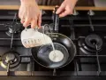 Mani versano panna da cucina in una padella su un fornello a gas.