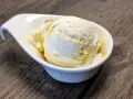Ein Löffel cremiges Buttermilch-Eis, beträufelt mit Honig, in einer weißen Schale auf Holztisch.
