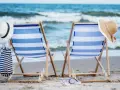 Dwa leżaki na plaży, gotowe na idealny weekend nad morzem. W tle szum fal i błękitne niebo.