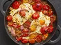 Heißer, gebackener Feta mit Kirschtomaten und roten Zwiebeln in einer Pfanne, mit Kräutern bestreut.
