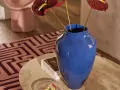 Niebieski wazon o intensywnym, **kolor chabrowy inaczej** odcieniu, z ciemnoczerwonymi anturium, stoi na marmurowym stoliku.