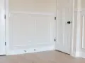A room with a DIY chair rail, wainscoting, and white doors. The walls are painted a light cream color.