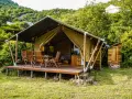 Glamping w Czarnogórze: namiot z drewnianym tarasem, stołem i krzesłami, otoczony zielenią. Idealne miejsce na relaks.