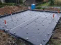 Fundament budowlany z folią i rurami. Widać małe kostki, które służą jako dystanse do zbrojenia, zapewniając odpowiednią grubość otuliny betonu.