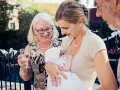 Elegancka mama karmi dziecko na chrzcinach. Babcia z kieliszkiem wina podziwia wnuka. Jak się ubrać na chrzciny? Klasycznie i z klasą.