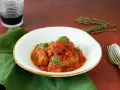 Involtini di carne in padella con sughetto, guarniti con basilico fresco, serviti in un piatto bianco su un tovagliolo verde.
