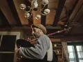 Mężczyzna w czapce gra na dudach, szkockim instrumencie, w przytulnym wnętrzu.
