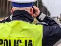 Policjant w kamizelce odblaskowej obserwuje drogę, gdzie widać ciężarówkę. Na drodze obowiązuje zakaz wyprzedzania dla ciężarówek.