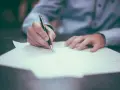 Dłoń pisze długopisem na papierze, finalizując wpis do księgi wieczystej.