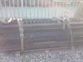Stos czarnych, metalowych elementów naczepy z pasami transportowymi.