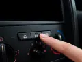 Finger presses the A/C button on a car's climate control panel, ready to activate the car air conditioning for a cool ride.