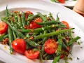 Insalata di fagiolini freschi con pomodorini ciliegino e erbe aromatiche, servita in un piatto bianco.