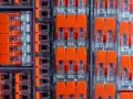 Zbliżenie na pomarańczowe złącza elektryczne w przezroczystych obudowach, ułożone w rzędy.
