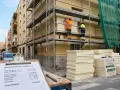 Presupuesto de obra SATE: dos trabajadores instalan aislamiento térmico en fachada. Materiales apilados y presupuesto detallado.