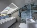 Bagno sottotetto basso con vasca, doccia con piastrelle blu marmorizzate e lucernario.