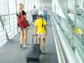 Młoda kobieta z plecakiem i dziewczynka z walizką idą korytarzem lotniska. To może być ich wyjazd nieletniego za granicę bez rodziców.