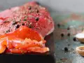 Un filet de gravlax de truite, assaisonné de poivre et d'herbes, prêt à être dégusté. Deux cuillères en bois contiennent sel et genièvre.
