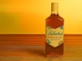 Butelka Ballantines Sweet Blend na drewnianym blacie, w tle ciepłe, żółte światło.