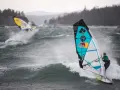 Windsurferzy na falach, jeden z nich na pierwszym planie, w akcji.