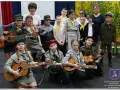 Dzieci w strojach harcerskich grają na gitarach i mandolinie. To może być zapowiedź piosenki o harnasiu.