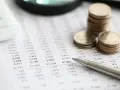 Monedas apiladas sobre un informe financiero, con una calculadora y un bolígrafo. El informe muestra números, quizás el modelo 420.