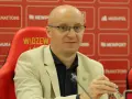 Nowy trener Widzewa w jasnej marynarce, siedzi na czerwonym fotelu z logo klubu.