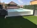 Moderna piscina con mosaico blanco, rodeada de césped artificial y setos. Ideal para decoración de terrazas con piscina.