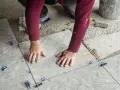 Mani esperte posano mattonelle con precisione, usando livellatori per un risultato perfetto.