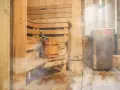 Drewniana sauna z piecem, ławami i wiaderkiem z miotełką. Idealne miejsce, by dowiedzieć się, jak zbudować saunę i odpocząć.