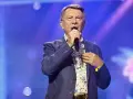 Wojciech Gąsowski w niebieskiej marynarce w kropki i kwiecistej koszuli śpiewa na scenie.