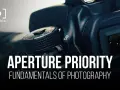 Gros plan sur un appareil photo, avec le texte "APERTURE PRIORITY" et "FUNDAMENTALS OF PHOTOGRAPHY". Le mode priorité ouverture est essentiel pour maîtriser la profondeur de champ.