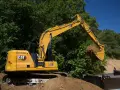 Żółta koparka Cat 313 z łyżką pełną ziemi, gotowa do pracy. Dane techniczne tej maszyny budowlanej są imponujące.