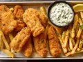 Idealny Fish and Chips przepis: chrupiące ryby w panierce, złociste frytki, sos tatarski i cytryna na tacy.