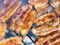 Kawałki soczystego boczku surowego pieką się na grillu, otoczone dymem.