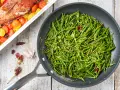 Asparagi di mare saltati in padella con aglio e peperoncino, accanto a un pesce al forno con pomodorini.