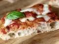 Fetta di pizza fatta in casa teglia, con crosta alveolata, pomodoro, mozzarella filante e una foglia di basilico fresco.