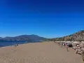 Słoneczna plaża w Sarigerme, z turkusowym morzem, górami w tle i rzędami leżaków pod słomianymi parasolami.