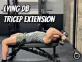 Man utför liggande tricepsextension med hantlar på en träningsbänk i ett gym.