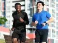 Deux hommes souriants courent ensemble dans un parc, profitant de leur routine pour courir tous les jours.
