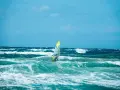 Windsurfer na wzburzonym, turkusowym morzu pod błękitnym niebem.