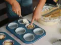 Dziecko nakłada ciasto na muffinki łyżką do formy.