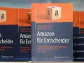 Bücher "Amazon für Entscheider" mit Amazon-Logo-Würfel im Vordergrund.