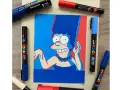 Un dessin de Marge Simpson réalisé avec des feutres Posca, entouré de plusieurs marqueurs Posca de différentes couleurs.