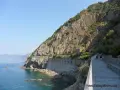 Wanderer auf dem Sentiero Azzurro entlang der felsigen Küste Liguriens. Das Meer glitzert türkisblau neben dem steilen Hang.