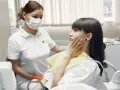 Pacjentka z bólem zęba w gabinecie dentystycznym, lekarka w masce ją bada.